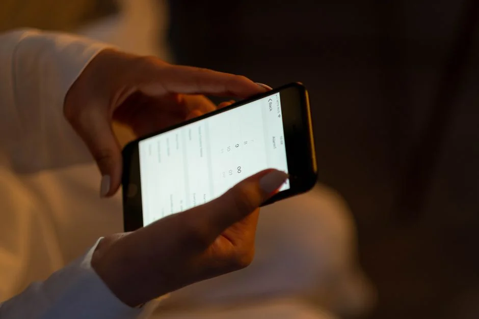 Woman using smartphone for online shopping with credit card in hand, festive background lighting.